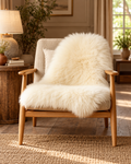 Single ivory sheepskin draped over an oak and linen armchair in a warm country-house interior
